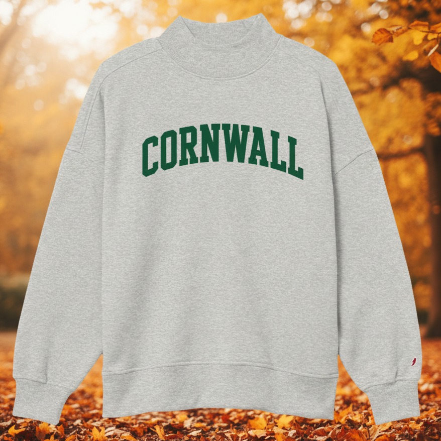 A light heather gray crewneck sweatshirt featuring the word 'CORNWALL' printed in dark green arched block letters across the chest, displayed on a clean white background.
